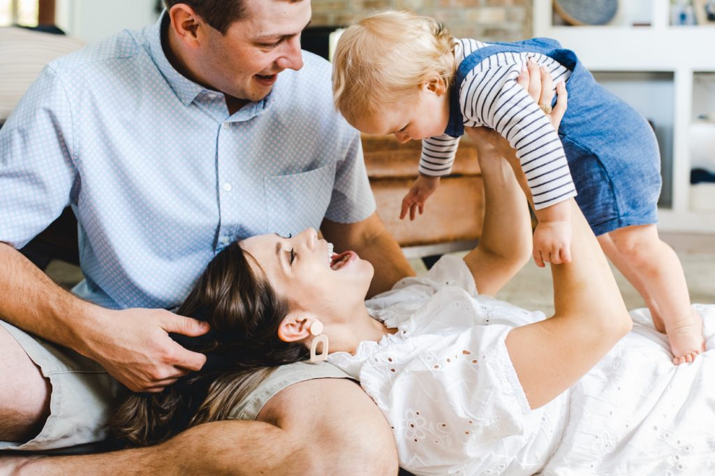 family playing with their toddler son in a light-filled living room at home during family photos