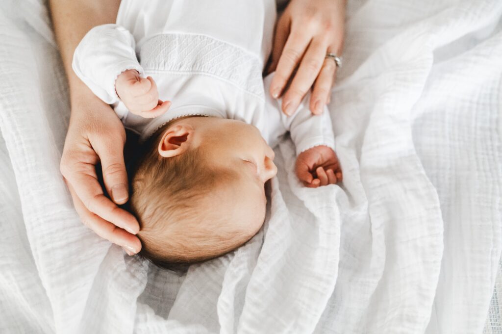 Image a newborn baby with mom's hands on baby's head - things to do for a new mom